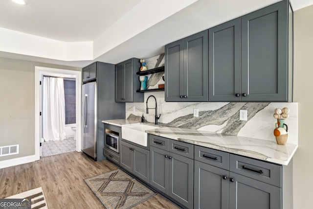 kitchen with light wood finished floors, open shelves, stainless steel appliances, visible vents, and a sink