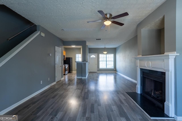 unfurnished living room featuring baseboards, visible vents, a ceiling fan, a fireplace with raised hearth, and dark wood-style flooring