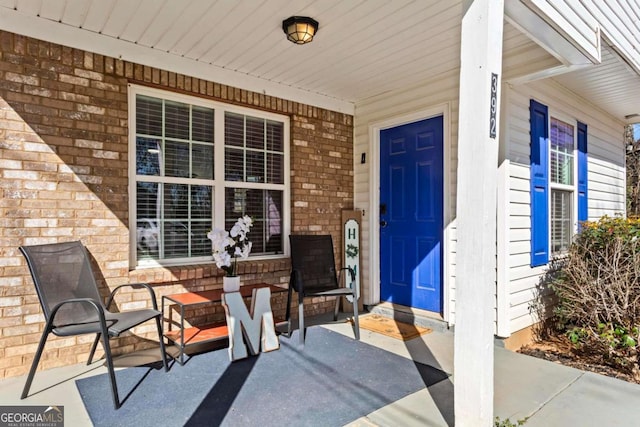 view of exterior entry with a porch and brick siding