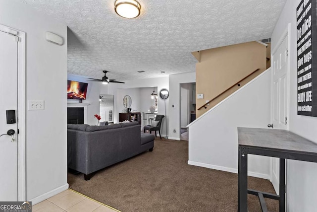 carpeted living area featuring a textured ceiling, a fireplace, a ceiling fan, baseboards, and stairs