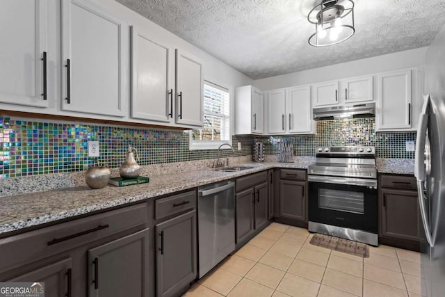 kitchen featuring stainless steel appliances, light tile patterned flooring, a sink, light stone countertops, and under cabinet range hood