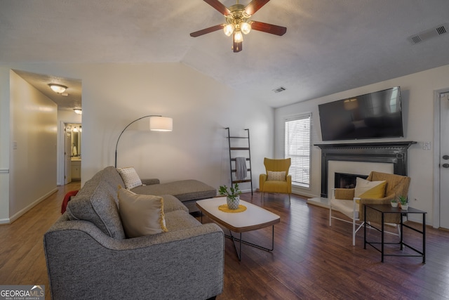 living area featuring vaulted ceiling, a fireplace with raised hearth, wood-type flooring, and visible vents