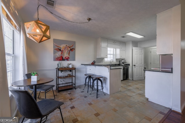 kitchen with visible vents, dark countertops, a kitchen breakfast bar, a peninsula, and white cabinetry