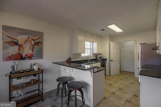 kitchen with a peninsula, a sink, visible vents, a kitchen breakfast bar, and white cabinets