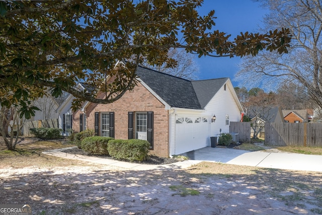 view of home's exterior with an attached garage, brick siding, fence, driveway, and roof with shingles