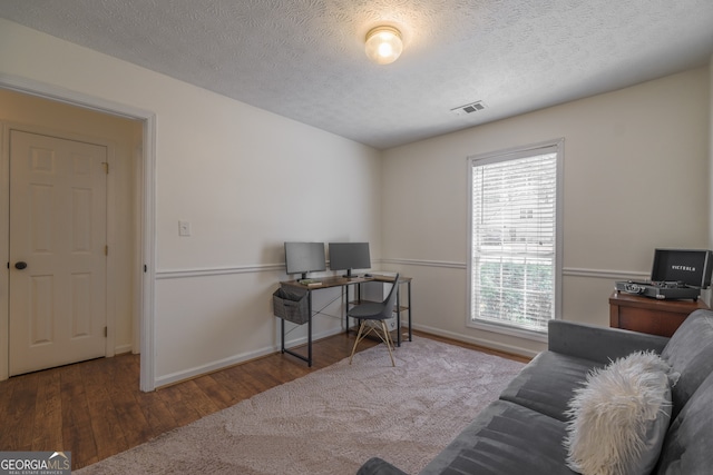 office space with visible vents, a textured ceiling, baseboards, and wood finished floors