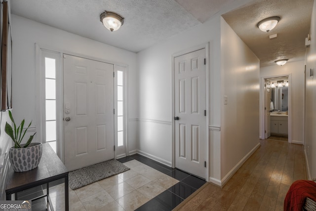 foyer entrance featuring hardwood / wood-style flooring, baseboards, and a textured ceiling