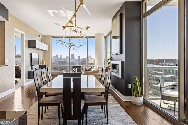 dining space with a chandelier, a city view, wood finished floors, baseboards, and expansive windows