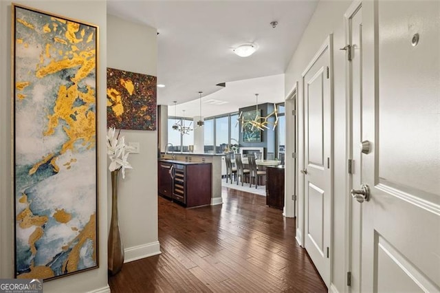 hall featuring a notable chandelier, dark wood finished floors, a sink, and beverage cooler