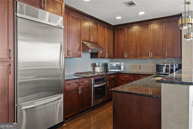 kitchen featuring dark wood-style flooring, visible vents, appliances with stainless steel finishes, dark stone countertops, and under cabinet range hood