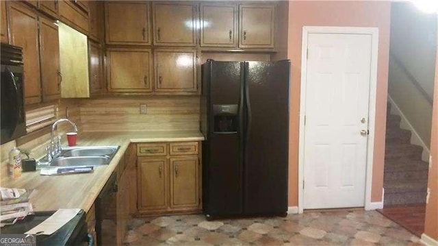 kitchen with brown cabinets, light countertops, black fridge with ice dispenser, a sink, and baseboards