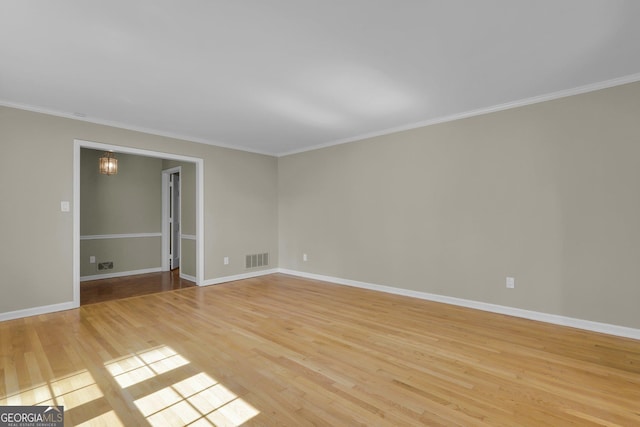 spare room featuring a notable chandelier, visible vents, ornamental molding, light wood-type flooring, and baseboards