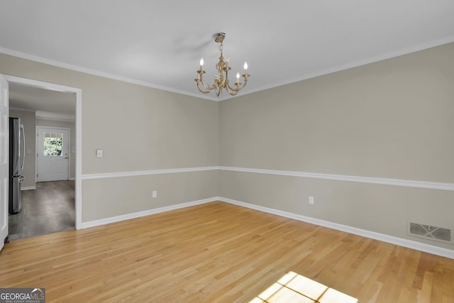 empty room with a chandelier, light wood-style flooring, visible vents, baseboards, and crown molding