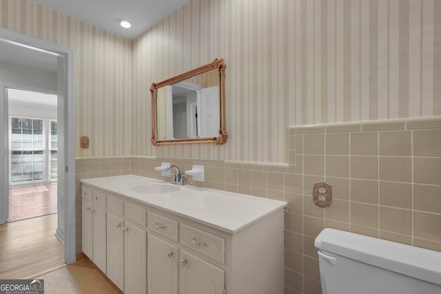 half bathroom featuring a wainscoted wall, vanity, toilet, and wallpapered walls