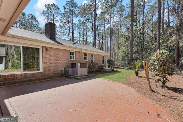 rear view of house featuring brick siding, roof with shingles, crawl space, a chimney, and a patio area