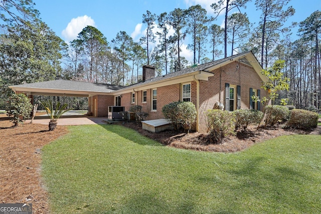 back of property featuring brick siding, a yard, driveway, a carport, and a chimney