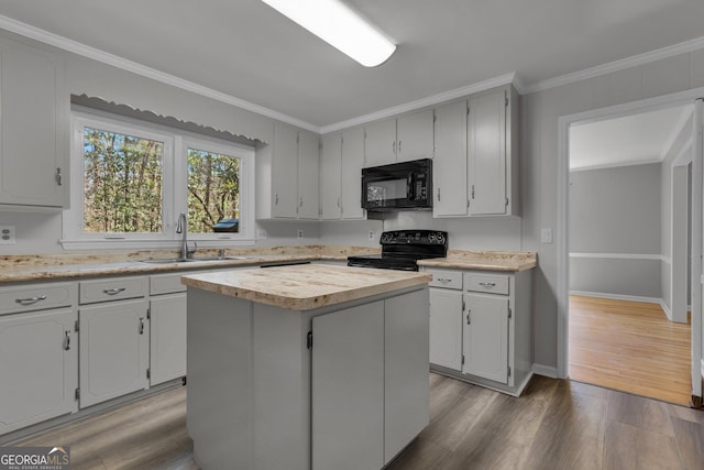 kitchen with light countertops, ornamental molding, a sink, wood finished floors, and black appliances