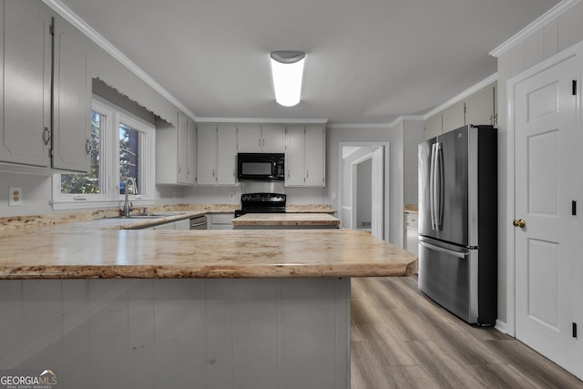 kitchen with a peninsula, wood finished floors, a sink, ornamental molding, and black appliances