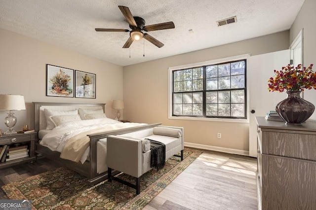 bedroom with a textured ceiling, ceiling fan, wood finished floors, visible vents, and baseboards