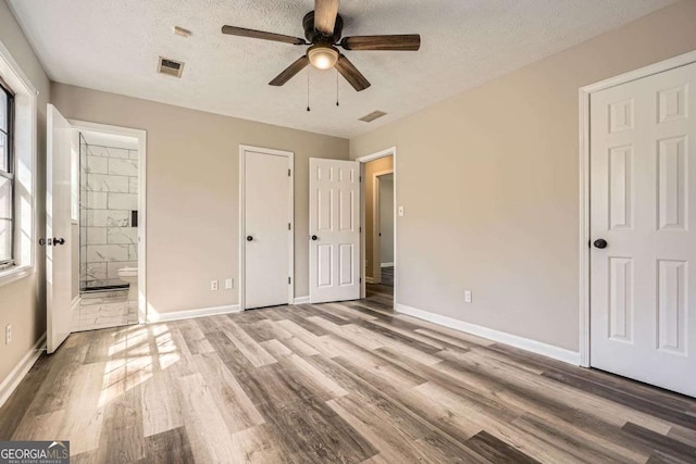 unfurnished bedroom with a textured ceiling, connected bathroom, wood finished floors, visible vents, and baseboards