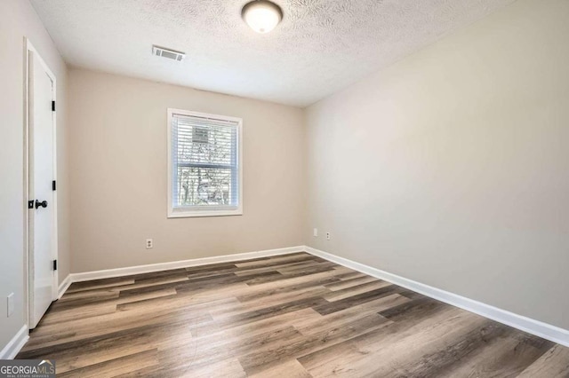 empty room featuring baseboards, a textured ceiling, visible vents, and wood finished floors