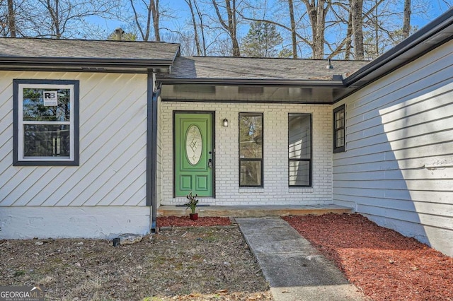 entrance to property featuring a shingled roof and brick siding