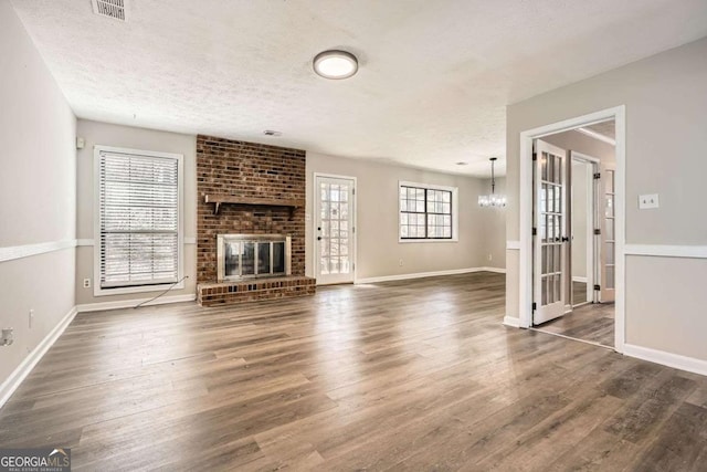 unfurnished living room featuring a brick fireplace, visible vents, a textured ceiling, and wood finished floors