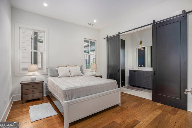 bedroom with a barn door, visible vents, baseboards, wood finished floors, and recessed lighting