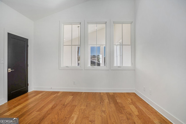 empty room with lofted ceiling, light wood-type flooring, and baseboards