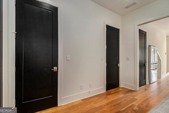 unfurnished bedroom with light wood-type flooring, freestanding refrigerator, visible vents, and baseboards