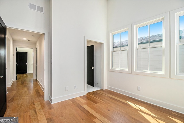 empty room featuring light wood-style floors, baseboards, visible vents, and a high ceiling