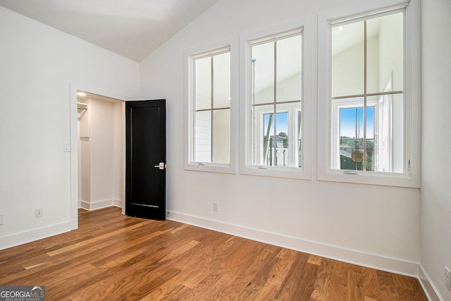 unfurnished room featuring a wealth of natural light, vaulted ceiling, baseboards, and wood finished floors