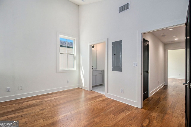 unfurnished bedroom featuring electric panel, baseboards, visible vents, wood finished floors, and ensuite bathroom