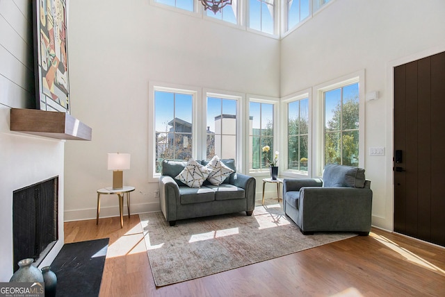 living room with a towering ceiling, a fireplace with flush hearth, baseboards, and wood finished floors