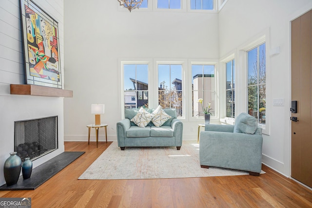 living area featuring a large fireplace, a towering ceiling, baseboards, and wood finished floors