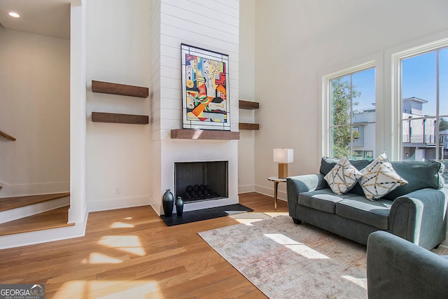 living room with recessed lighting, a fireplace, wood finished floors, a towering ceiling, and baseboards