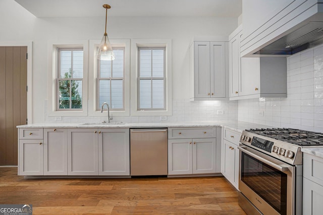 kitchen with light wood finished floors, stainless steel appliances, tasteful backsplash, a sink, and premium range hood