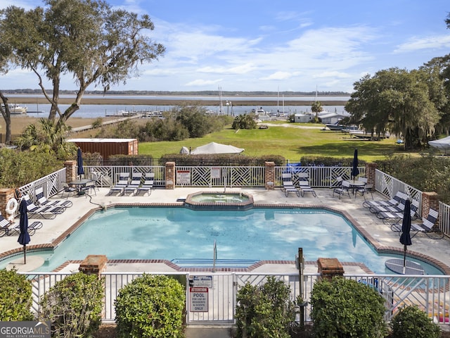 view of swimming pool featuring a water view, a patio area, a pool with connected hot tub, and fence