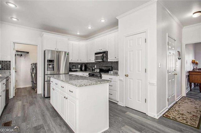 kitchen with dark wood-style flooring, stainless steel appliances, crown molding, white cabinetry, and backsplash