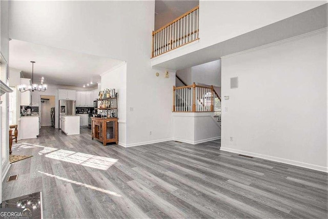 unfurnished living room featuring a notable chandelier, visible vents, stairway, wood finished floors, and baseboards