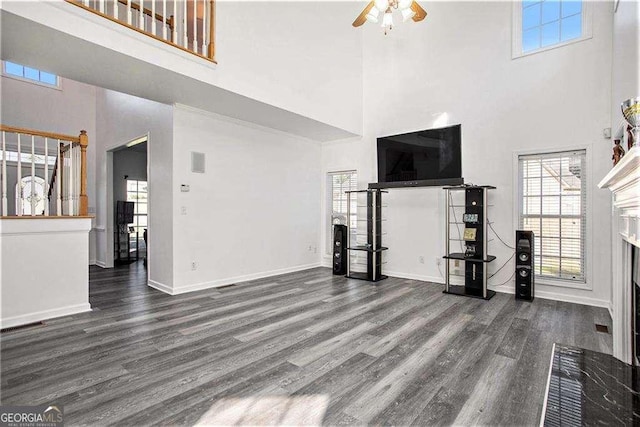 unfurnished living room with a towering ceiling, ceiling fan, baseboards, and dark wood-style flooring