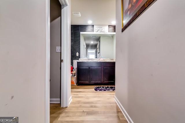 hall with a sink, visible vents, baseboards, and light wood-style flooring