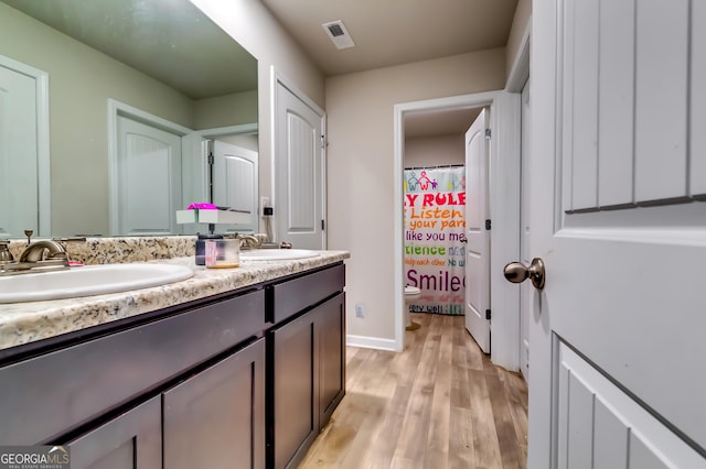 full bathroom with visible vents, toilet, a sink, wood finished floors, and double vanity