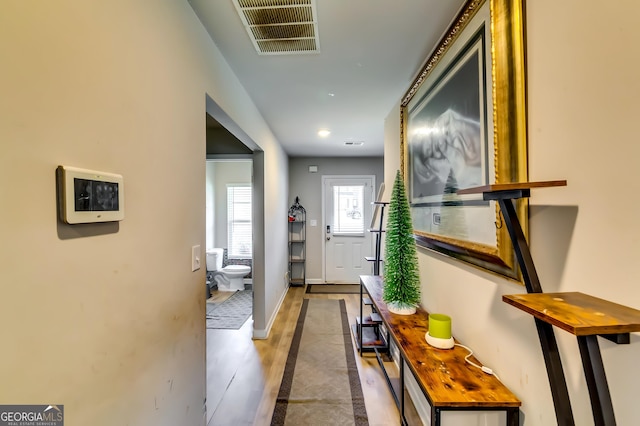 hall with visible vents, baseboards, and light wood finished floors