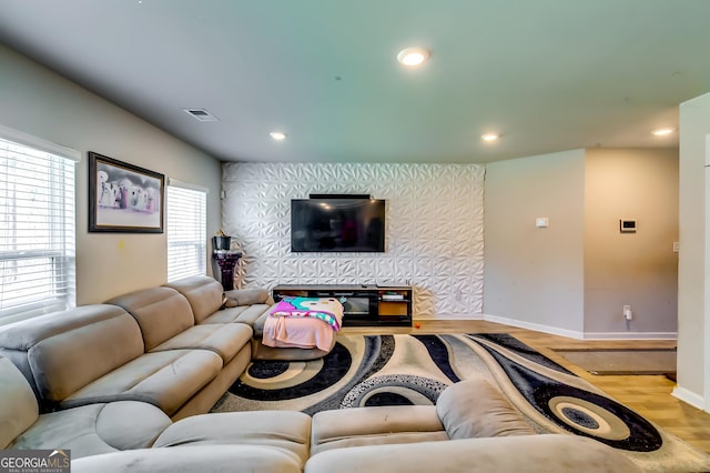 living room featuring wood finished floors, baseboards, visible vents, wallpapered walls, and an accent wall