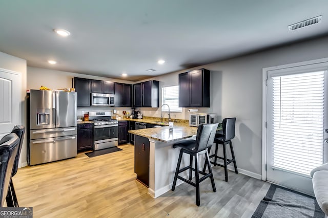 kitchen with visible vents, a breakfast bar, light stone counters, a peninsula, and stainless steel appliances