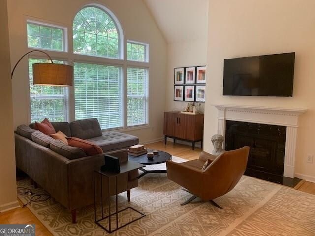 living room with baseboards, a fireplace with flush hearth, high vaulted ceiling, and wood finished floors