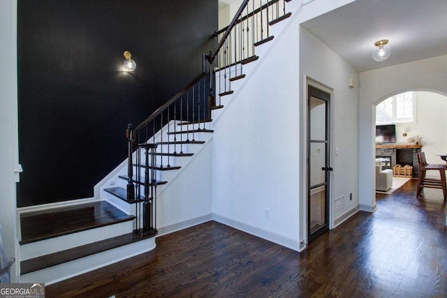 stairs with arched walkways, baseboards, and wood finished floors