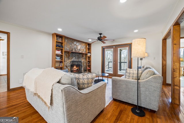 living room featuring hardwood / wood-style flooring, french doors, crown molding, and a stone fireplace