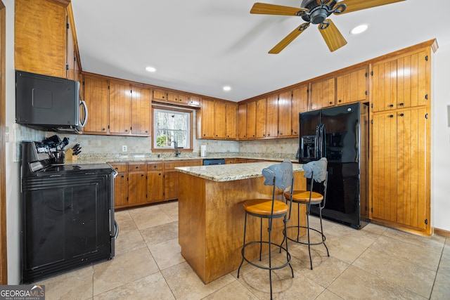 kitchen featuring brown cabinetry, a kitchen bar, black appliances, and tasteful backsplash